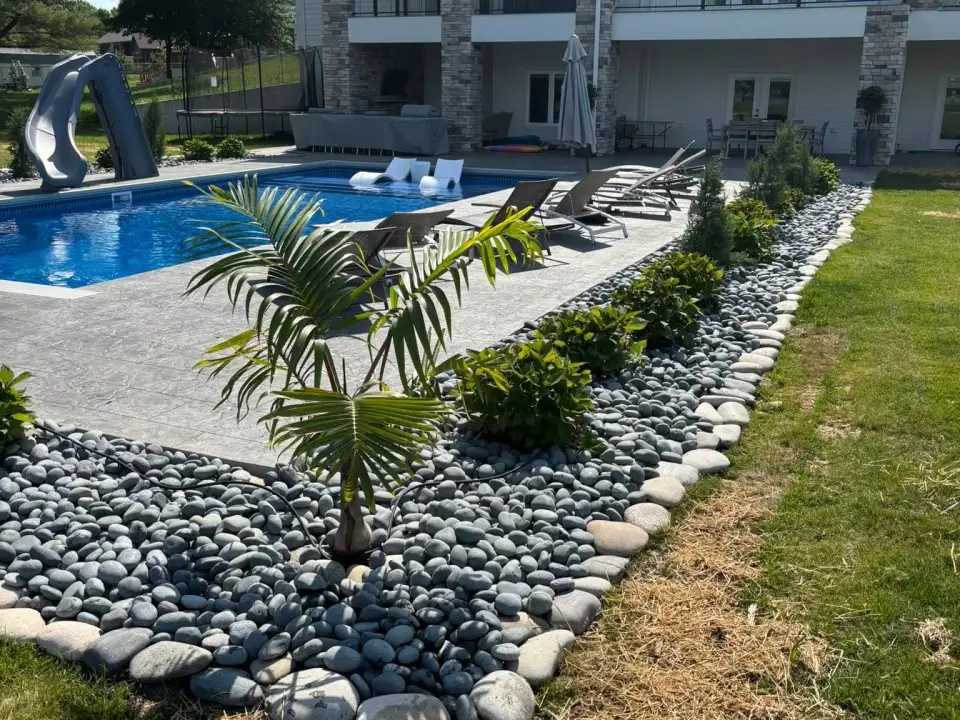 Planting bed with pale river rock beside a pool and lawn.