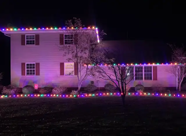 Multicolored lights line a two-story home and its front garden.