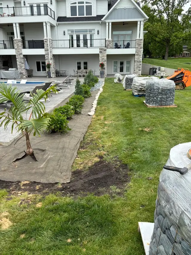 Plants and landscape fabric beside pallets of decorative stone.