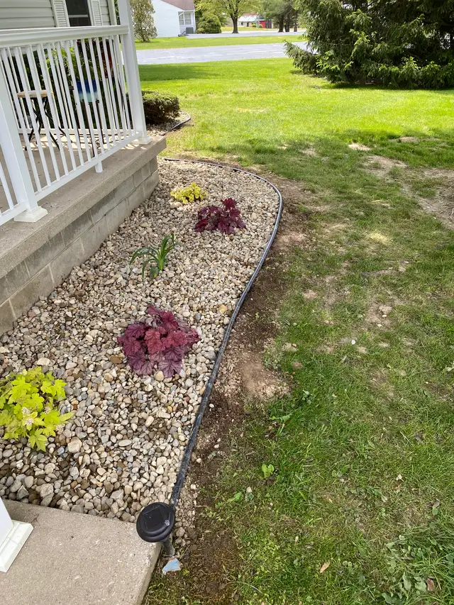 Small plants in a gravel bed beside a white porch railing.