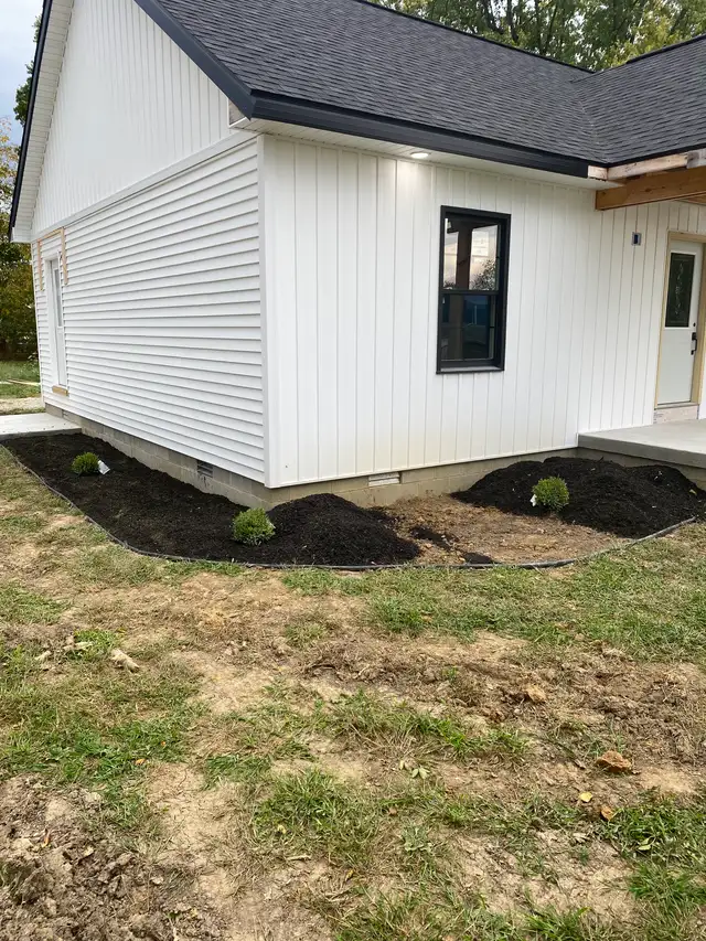 Dark mulch and planting around the corner of a white building.