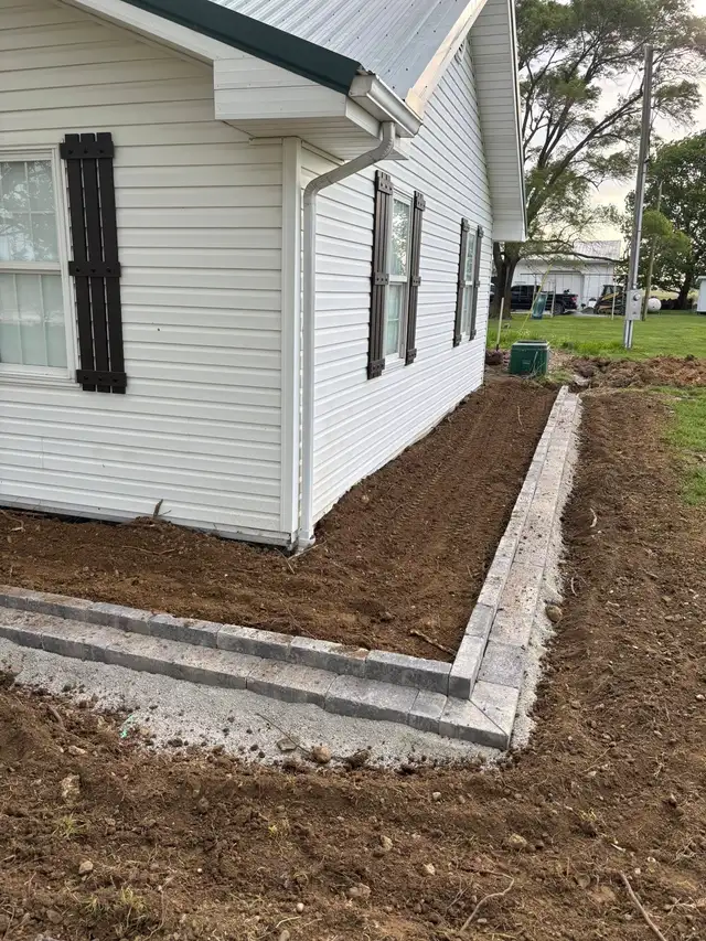 An edged garden bed around the corner of a white building.