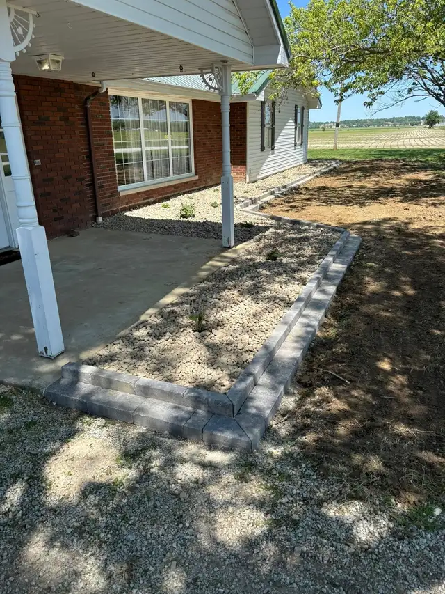 A curved stone-filled garden bed with small plants beside a porch.